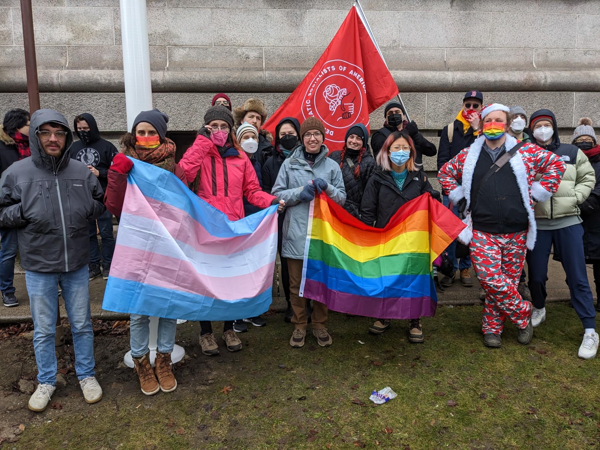 About 15 bembers of the Boston DSA contingent pose with a DSA flag and pride flags outside the Fall River Public Library