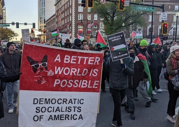 Protesters march through the streets of Boston holding signs that say "A Better World if Possible Democratic Socialists of America" and "Boston DSA Supports a Free Palestine"